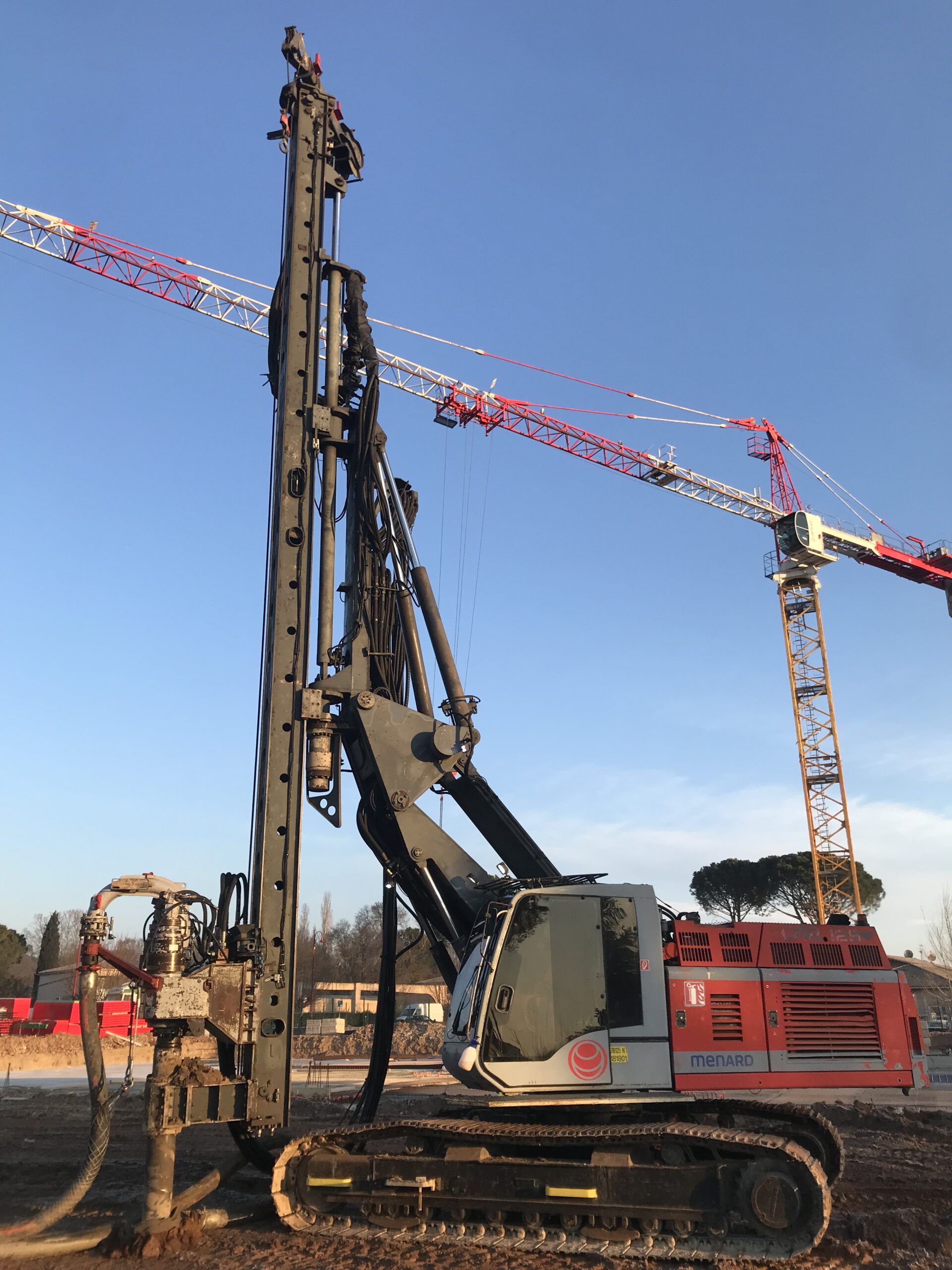 Menard intervient pour réaliser les fondations superficielles de bâtiments commerciaux. L'image représente la foreuse sur le chantier en premier plan.